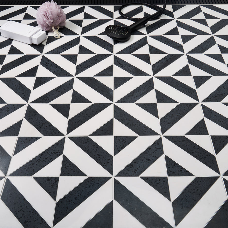 Black and white geometric patterned floor tiles with a shower head, a bar of soap, and a purple bath sponge placed on top.