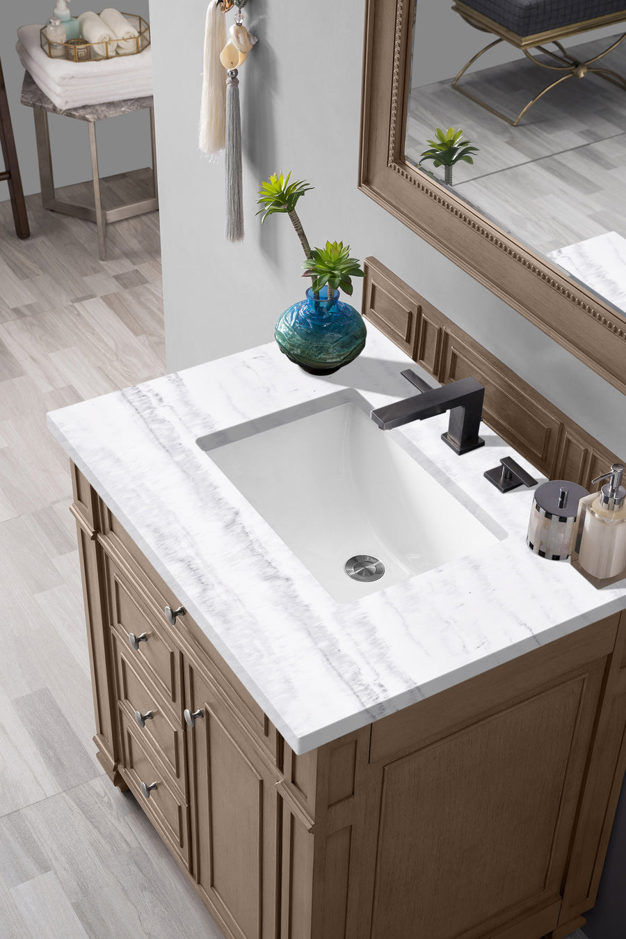 A bathroom vanity with a white marble countertop, rectangular sink, black faucet, soap dispenser, and a small green plant in a blue vase, seen from above. A mirror and part of the bathroom are also visible.