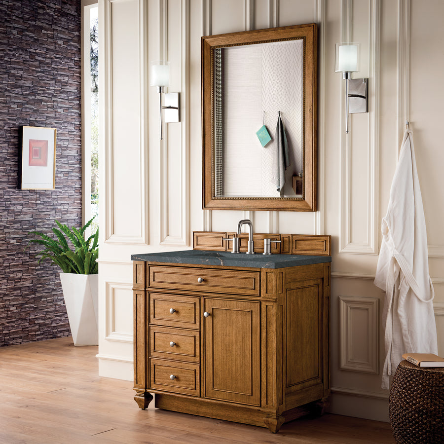 A bathroom with a wooden vanity, black countertop, large mirror, and two wall-mounted lights. There’s a robe hanging on the wall, a potted plant, and textured wallpaper with white paneling.