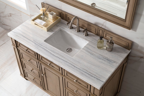 A bathroom vanity with a marble countertop, built-in sink, and brushed metal faucet. On the left, a tray holds toiletries and a towel; on the right, two soap dispensers are beside the sink. A large mirror is above the vanity.