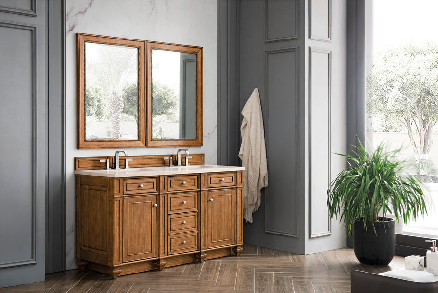 A bathroom with a wooden double-sink vanity, two mirrors, gray paneled walls, a towel hanging on a hook, a potted plant, and large windows showing greenery outside.