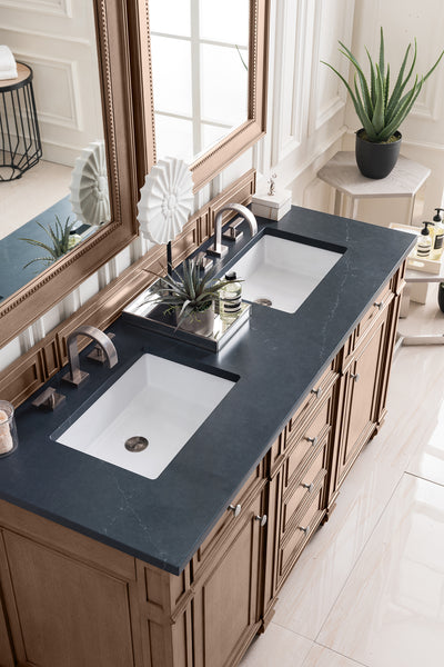 Double bathroom vanity with a black countertop, two white sinks, bronze fixtures, a large mirror, potted plants, and toiletries arranged neatly; natural light streams in from a nearby window.