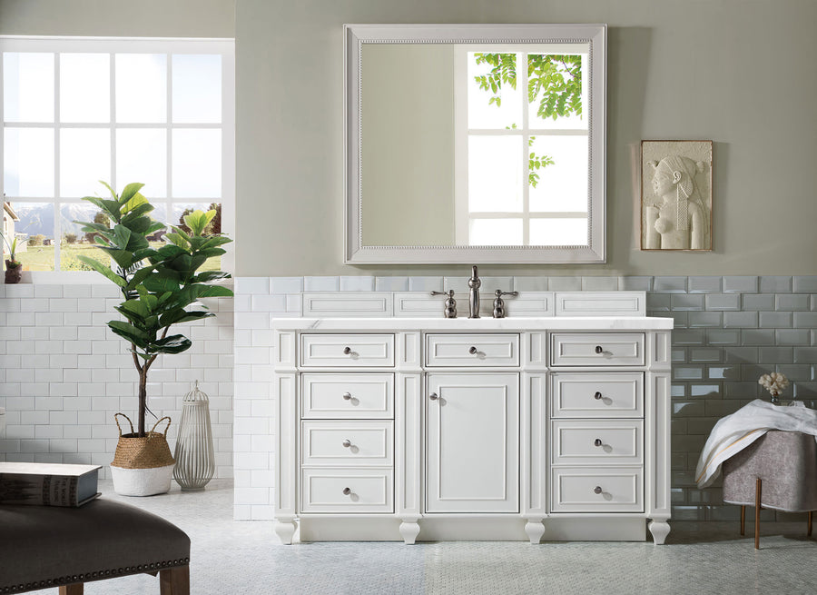 A bright luxury bathroom showcases a Bristol 60" Vanity with a large mirror above, silver fixtures, white subway tiles, a leafy potted plant, and a towel on a wooden stool as sunlight pours in through two windows.