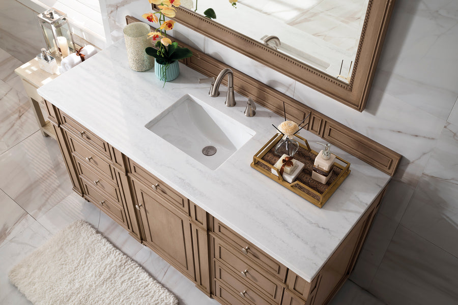 A bathroom vanity with a white marble countertop, built-in sink, silver faucet, toiletries on a tray, potted orchid, and large mirror above. The vanity is wood and the floor is tile with a white rug.