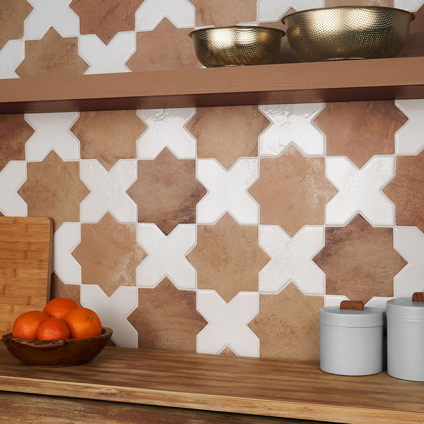 A kitchen counter with a wooden bowl of oranges, two white canisters, a cutting board, and a shelf holding two textured metal bowls. The backsplash features geometric star-shaped tiles in brown and white tones.