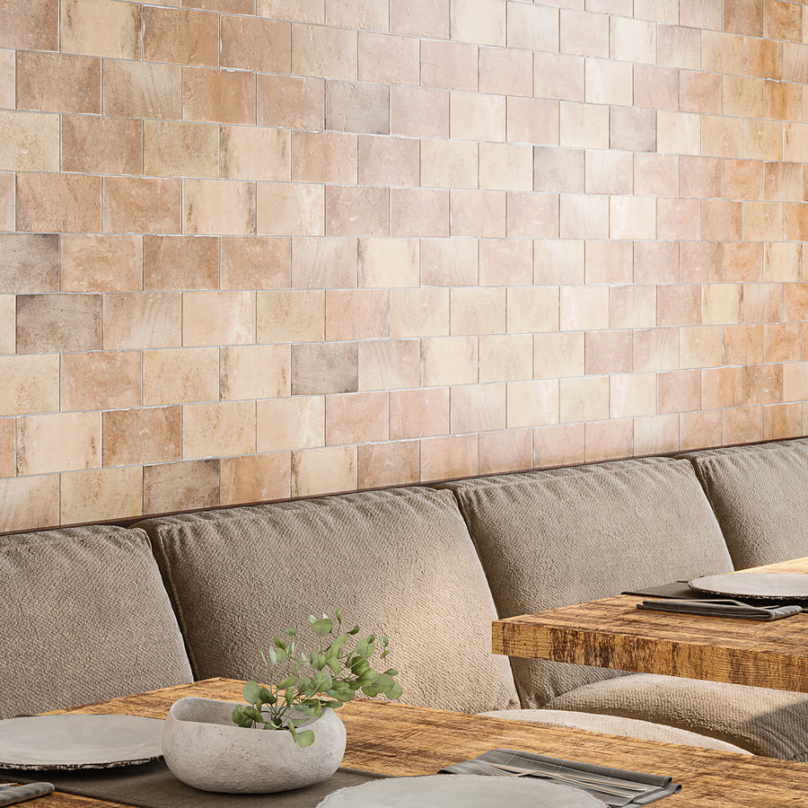 Cozy seating area with a textured beige sofa, rustic wooden table set with plates, and a beige ceramic pot holding green foliage; the wall is covered with rectangular tan tiles.
