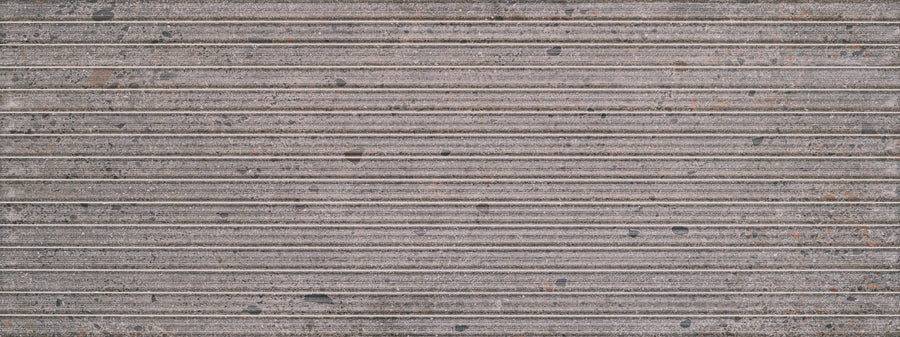 Close-up of Strata 18" x 48" Deco Tile in Earthen shows a textured surface with vertical, evenly spaced grooves. The linear pattern features worn areas accented by scattered dark spots and rust-like discolorations.