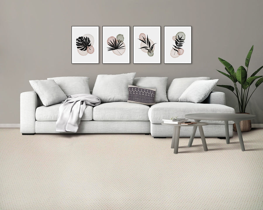 A modern living room with a light gray sofa, decorative pillows, a throw blanket, two round gray coffee tables, a potted plant, and three framed abstract botanical prints on a beige wall.