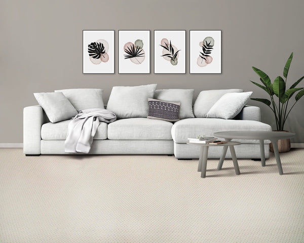A modern living room with a light gray sofa, decorative pillows, a throw blanket, two round gray coffee tables, a potted plant, and three framed abstract botanical prints on a beige wall.