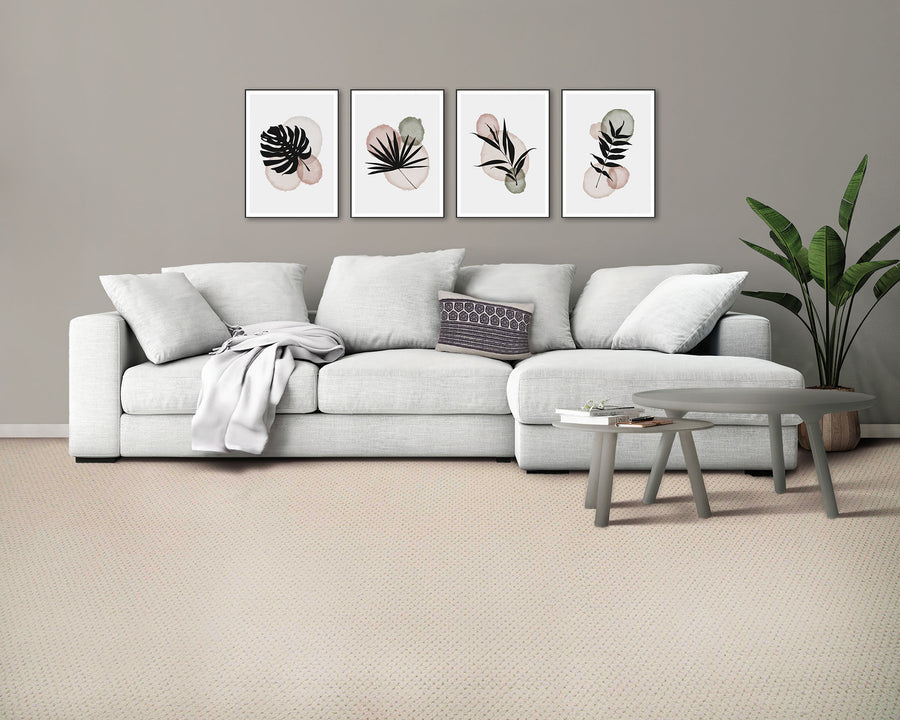 A modern living room with a light gray sofa, assorted cushions, a gray throw blanket, two round gray coffee tables, a potted plant, and three abstract botanical prints on a taupe wall above the sofa.