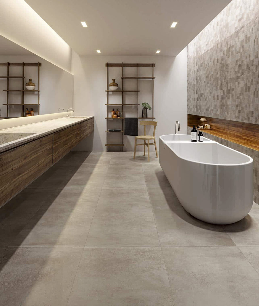 Modern bathroom with a large freestanding bathtub, floating wood vanity with double sinks, open shelving with decor, a wooden stool, and gray tile flooring and walls. The space is minimal and well-lit.