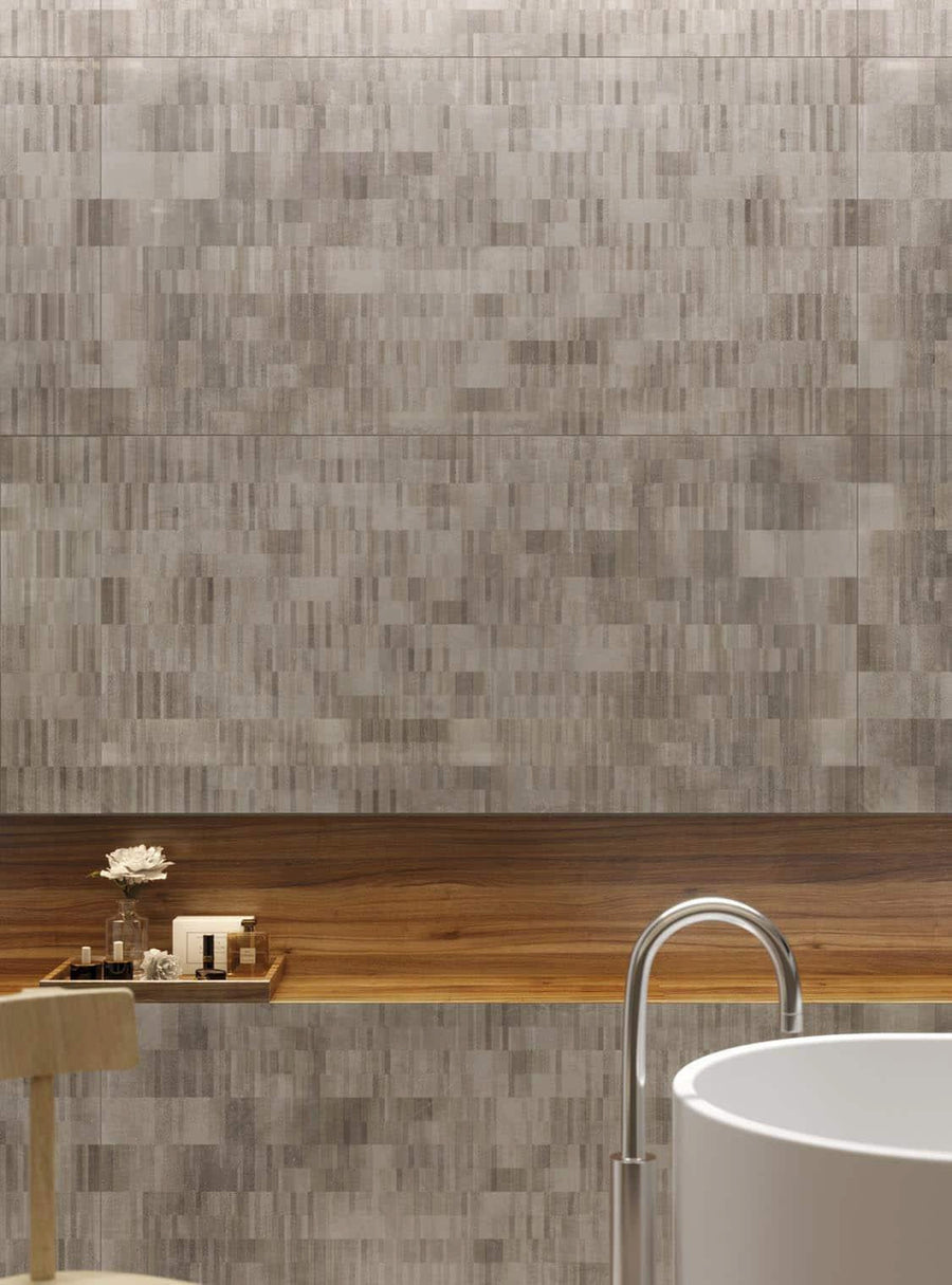 A modern bathroom features a round white bathtub, a light wooden chair, and a wooden shelf with decorative items, against a wall with textured, rectangular gray tiles.