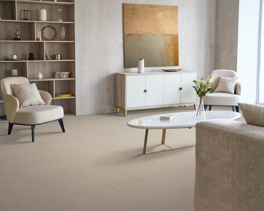 Modern living room with beige carpet, two cream armchairs, a sofa, a white oval coffee table with gold legs, a white sideboard, shelves with decor, a gold abstract painting, and a vase of flowers on the table.