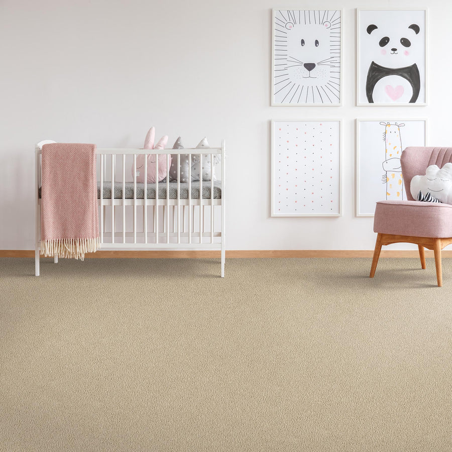 A nursery with a white crib, pink blanket, plush toys, light pink armchair, and four animal-themed art prints on a white wall. The floor is carpeted in beige. The decor is soft and pastel-toned.