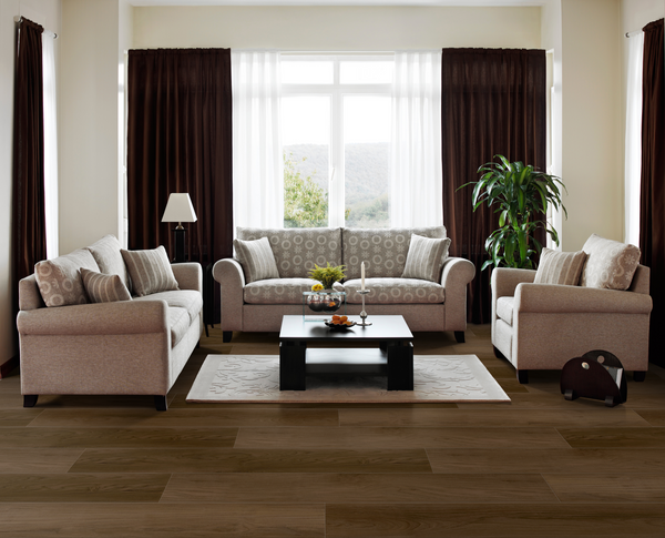 A modern living room with beige sofas, a dark coffee table, decorative pillows, a white rug, floor lamp, potted plant, and large window with brown curtains letting in natural light.