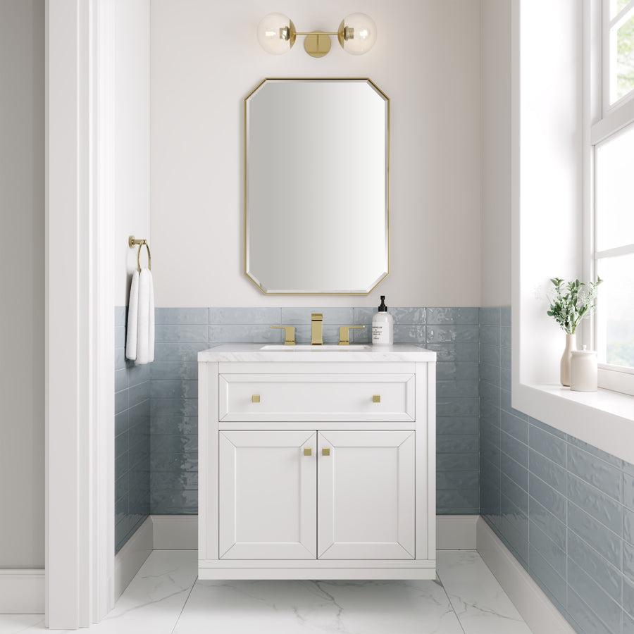 A small, modern bathroom with a Chicago 30" Vanity, gold fixtures, rectangular mirror, globe light, blue wall tiles, marble floor, window bringing in natural light, and a small plant on the windowsill.