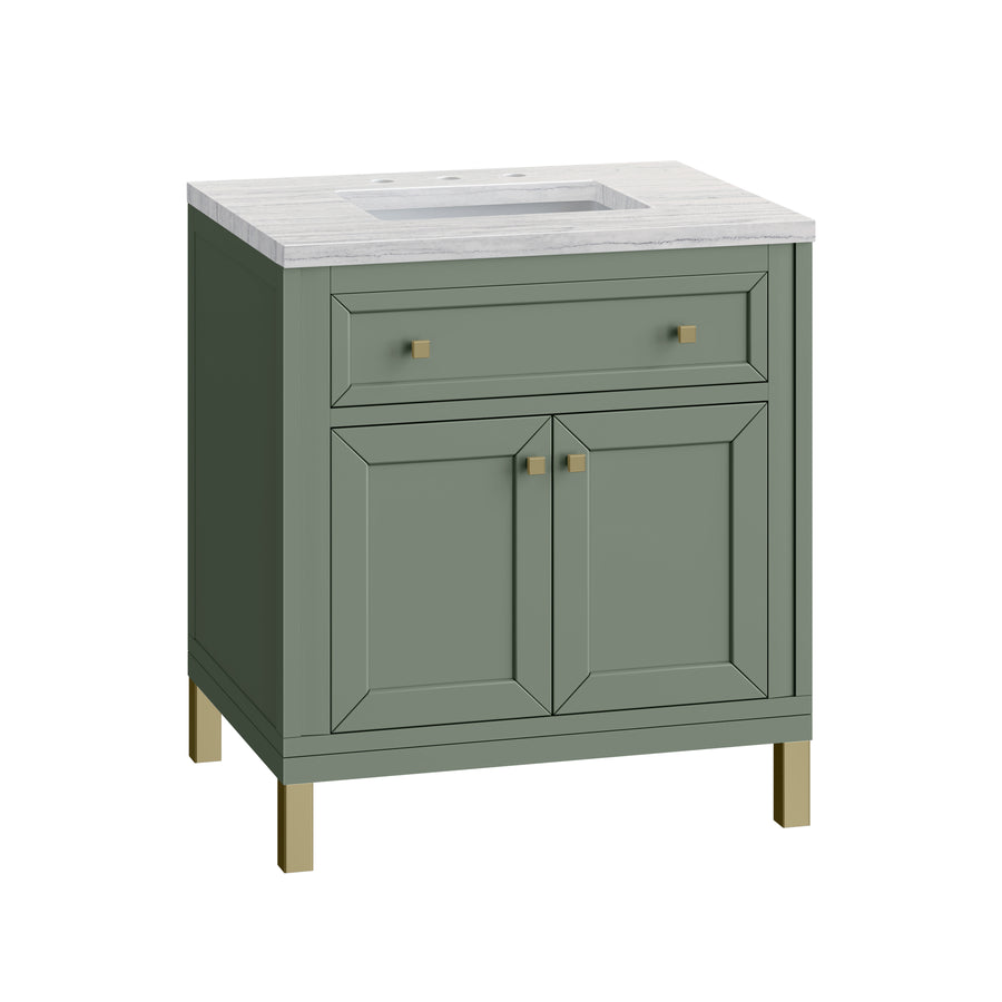 A green bathroom vanity with a white countertop, built-in sink, two cabinet doors, a top drawer, and gold-colored handles and leg accents.