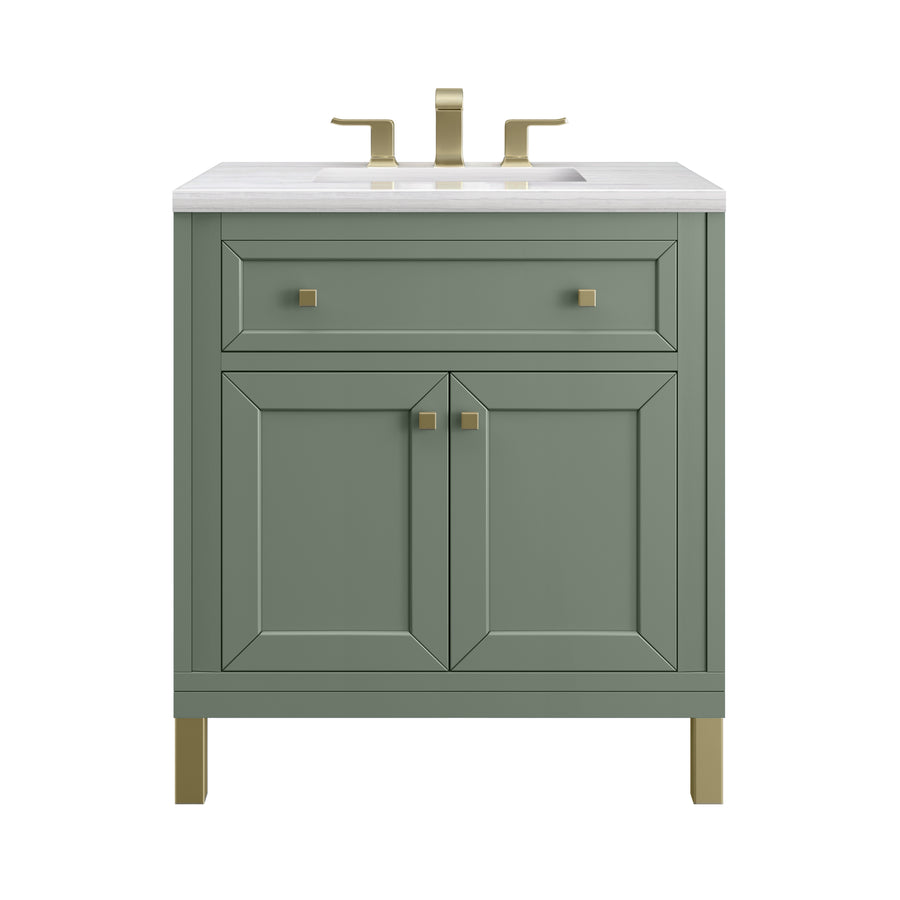 A green bathroom vanity with gold hardware and legs, featuring a white countertop, a rectangular sink, one wide top drawer, and two cabinet doors below. A gold faucet is mounted on the countertop.