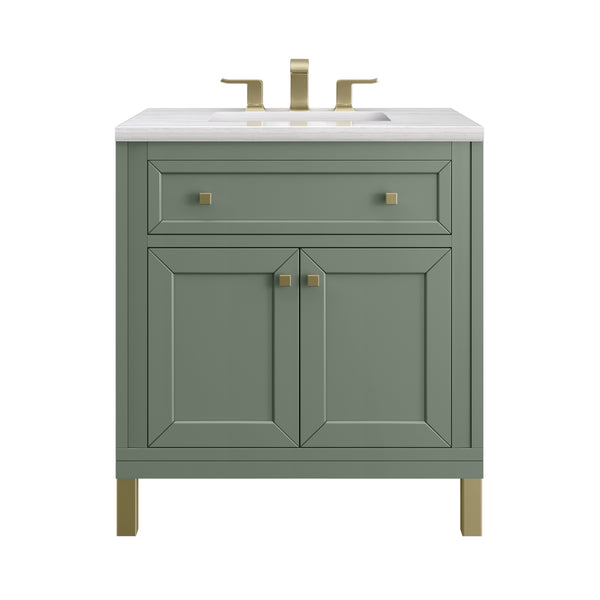 A green bathroom vanity with gold hardware and legs, featuring a white countertop, a rectangular sink, one wide top drawer, and two cabinet doors below. A gold faucet is mounted on the countertop.