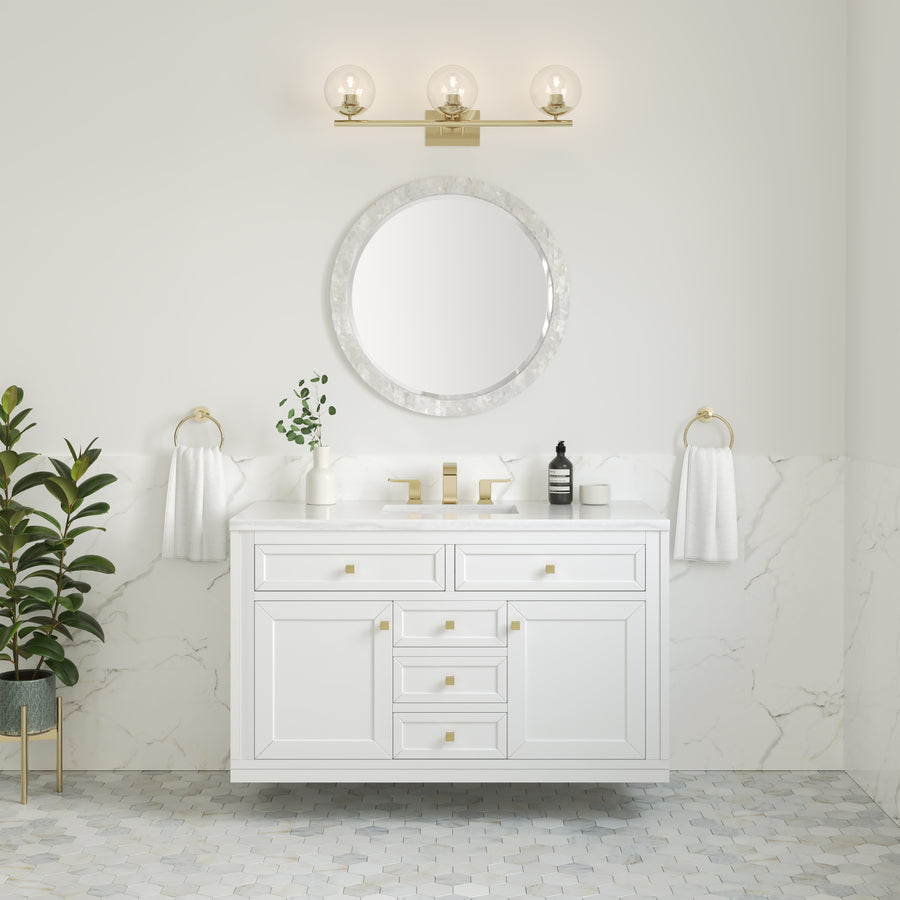 A modern bathroom with a Chicago 48" Vanity and marble top, round mirror, gold fixtures, wall sconces, two white hand towels, a potted plant on the left, and white marble walls with hexagon tile flooring.