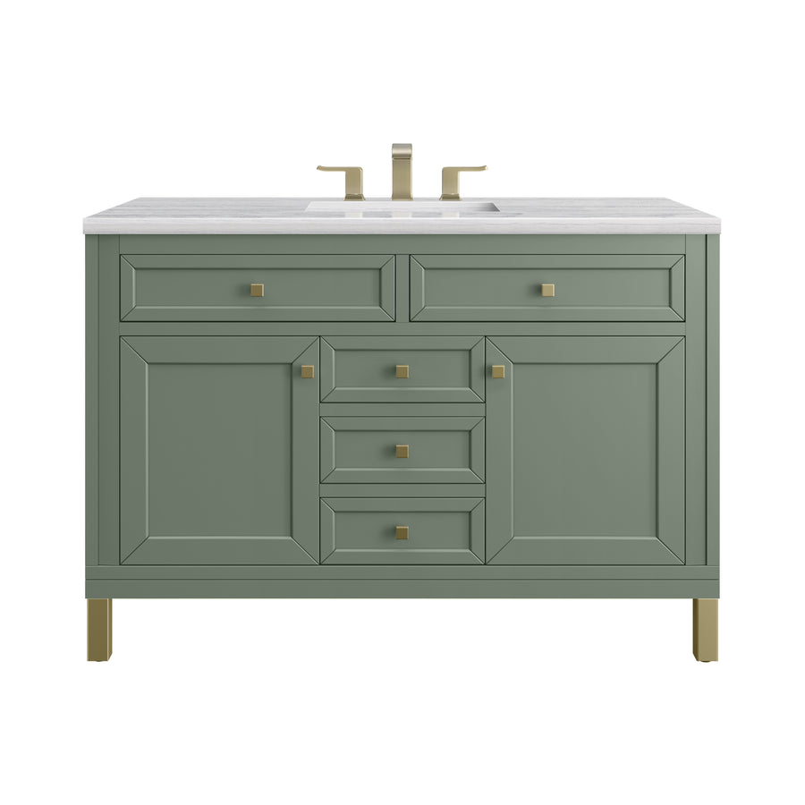 A sage green bathroom vanity with gold hardware, four central drawers, two side cabinets, and a white countertop featuring a built-in sink and gold faucet.