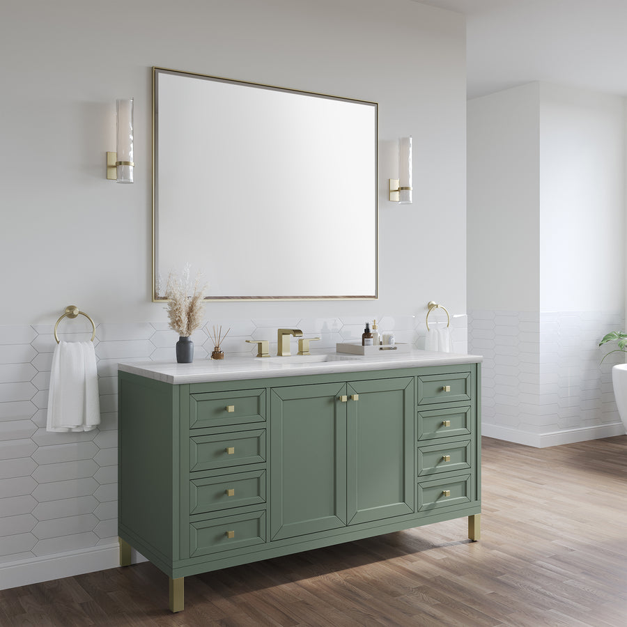 A modern bathroom with a sage green vanity, gold hardware, a large rectangular mirror, white countertop, wall sconces, decorative items, and towels on gold rings, set against white hexagonal tile and light walls.