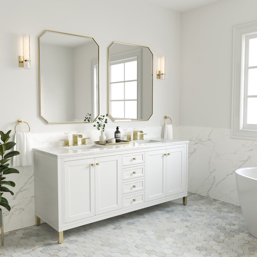 Modern bathroom with a white vanity, gold hardware, dual mirrors, marble countertop, wall sconces, a plant, and a hexagonal tile floor. Natural light comes through two windows, creating a bright, clean look.