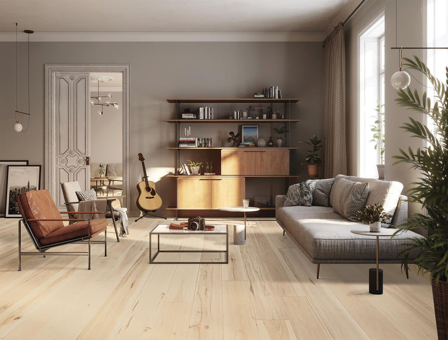 A modern living room with light wood floors, a gray sofa, a brown leather chair, a coffee table, a guitar, plants, bookshelves, and sunlight streaming through large windows.