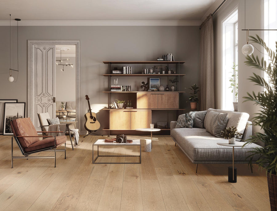 Modern living room with light wood flooring, a gray sofa, brown leather chair, coffee table, shelving unit with books and plants, a guitar, large windows, and neutral décor. Sunlight streams in, creating a cozy, inviting space.