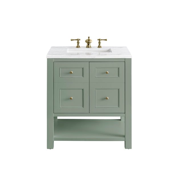 A light green bathroom vanity with a white marble countertop, brass faucet, four square drawer fronts with brass knobs, and an open lower shelf.