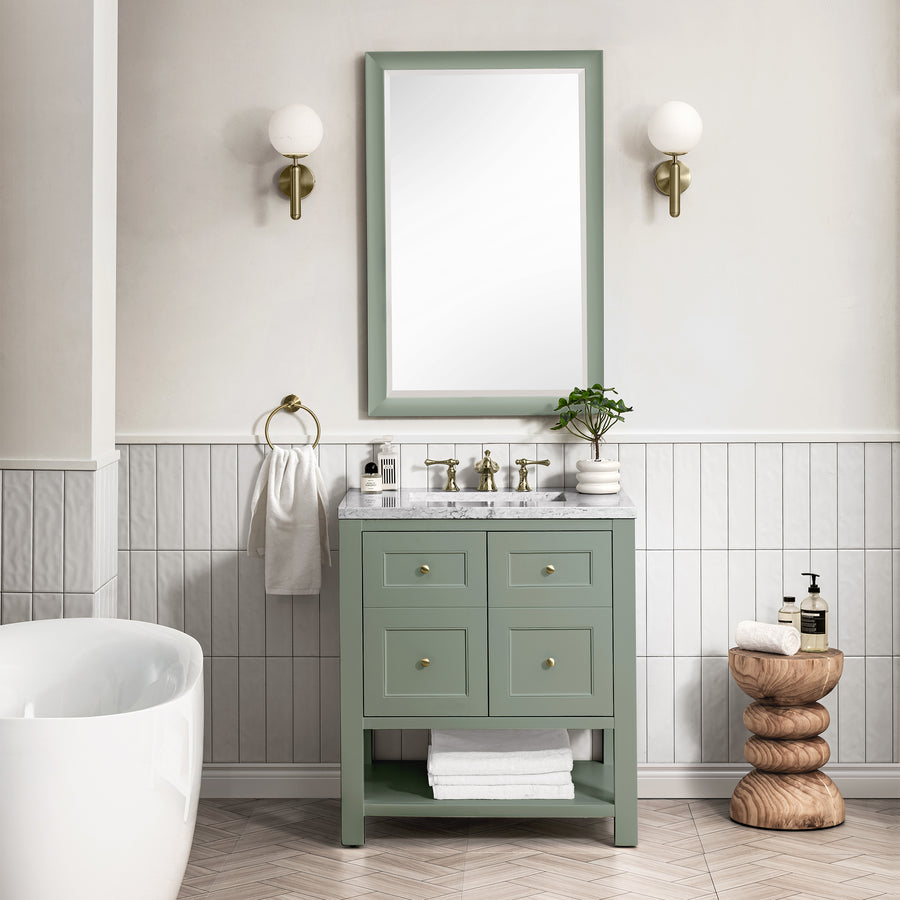 A bathroom featuring the Breckenridge 30" Vanity in green with a marble countertop, large mirror, two wall sconces, white bathtub, stacked wood stool, vertical white tile walls, and neatly arranged towels and toiletries.
