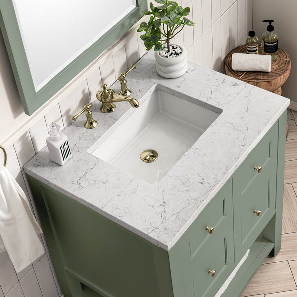 A bathroom vanity with a white and gray marble countertop, sage green cabinet, gold faucet, potted plant, soap dispenser, and toiletries on a small wooden stool beside it.