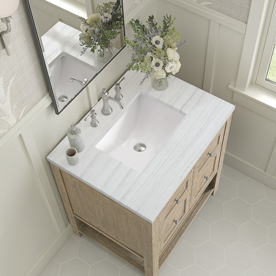 A bathroom vanity with a white marble countertop, built-in sink, silver faucet, small soap dispenser, cup, and a glass vase holding a bouquet of white and green flowers, seen from above.
