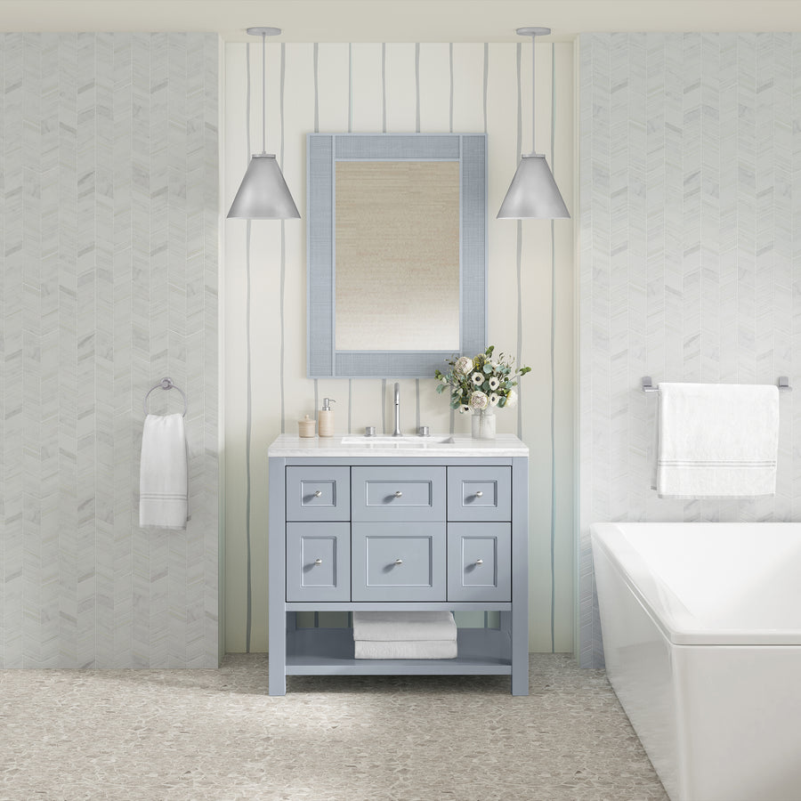 A modern bathroom with a light blue Breckenridge 36" Vanity, rectangular mirror, pendant lights, bathtub, towel racks, and flowers, set against light patterned walls and a textured floor in a transitional style.