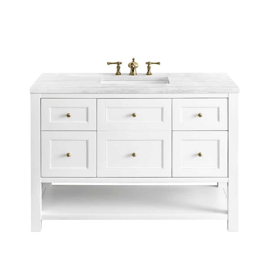 White bathroom vanity with a marble countertop, brass sink fixtures, and six drawers. The vanity has a lower open shelf and a rectangular undermount sink in the center.