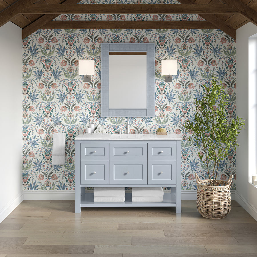 A bathroom features floral wallpaper, the Breckenridge 48" Vanity in light blue with drawers, a mirror, wall sconces, a potted plant, towels on a wooden shelf, and exposed wood ceiling beams that add luxury craftsmanship.