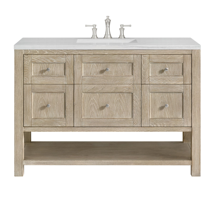 Light wood bathroom vanity with a white countertop, integrated sink, silver faucet, six drawers with silver knobs, and an open lower shelf.