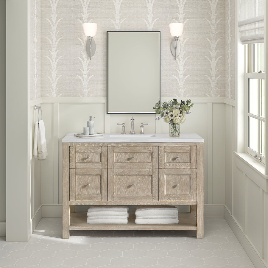 A bathroom features the Breckenridge 48" Vanity with a light wood finish, marble countertop, and six drawers. Towels sit on the lower shelf near a flower vase. A large mirror, sconces, and patterned walls enhance the transitional style.
