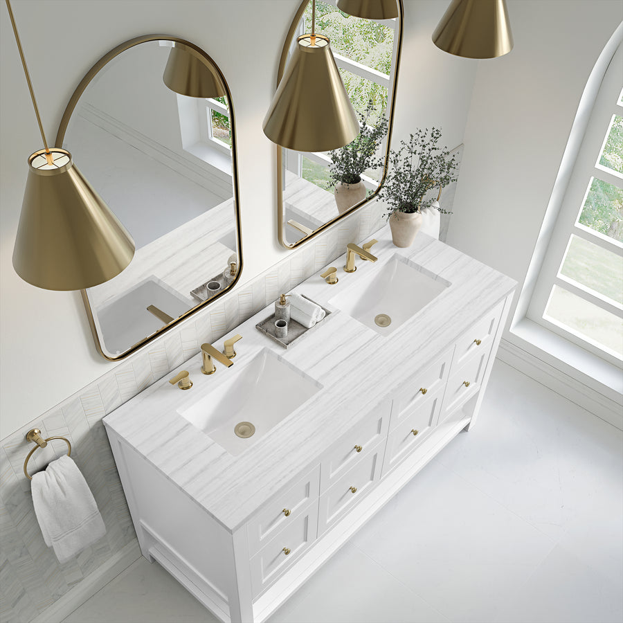 Modern bathroom with a double white marble sink vanity, gold fixtures, two large mirrors, gold pendant lights, and a white vase with greenery on a bright, sunlit white floor.