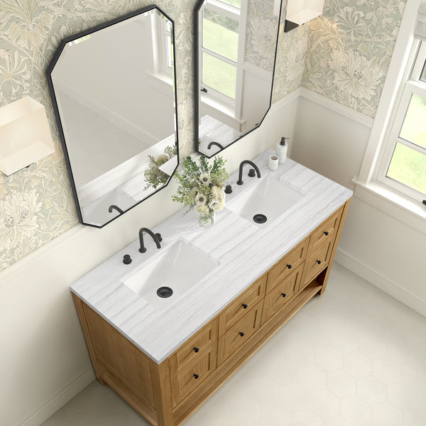 A bathroom vanity with a white marble countertop, two sinks with black faucets, a vase of flowers in the center, wood cabinetry, and two octagonal mirrors above, set against floral wallpaper and a hexagonal tile floor.