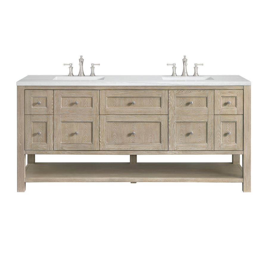 A double sink bathroom vanity with a light wood finish, six drawers, four smaller side drawers, two cabinets, a lower open shelf, and two sets of silver faucets on a white countertop.