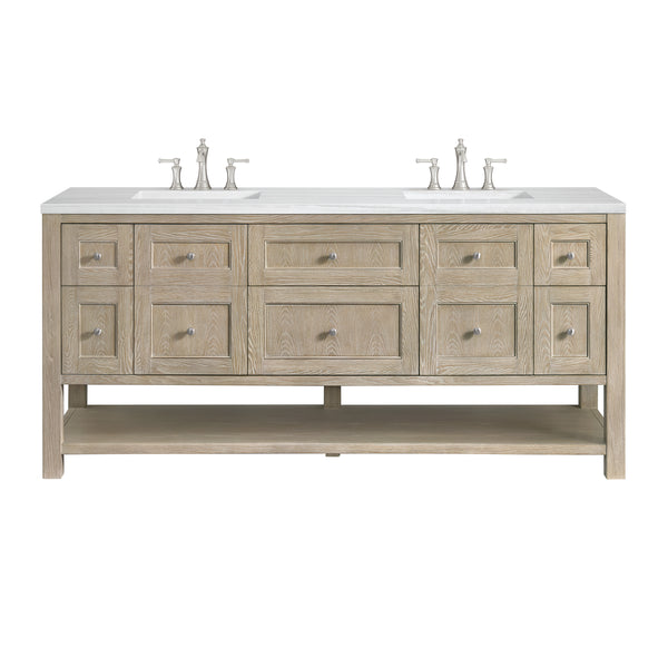 A double sink bathroom vanity with a light wood finish, six drawers, four smaller side drawers, two cabinets, a lower open shelf, and two sets of silver faucets on a white countertop.