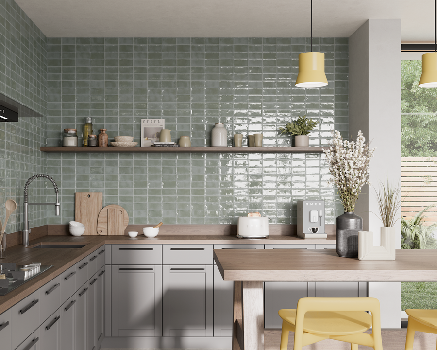 Modern kitchen with green tile backsplash, gray cabinets, wooden countertops, and open shelves holding jars and dishes. A yellow chair sits by a breakfast bar, and a window shows a garden outside.