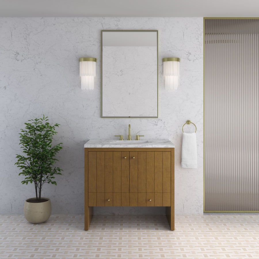 A modern bathroom featuring a striking Hudson 36″ Vanity in Honey Oak with a marble countertop, complemented by a mirror, two wall sconces, a potted plant, and a white towel hanging on a ring. The light-colored walls with subtle patterns enhance the luxury bathroom furniture, creating an elegant and inviting atmosphere.