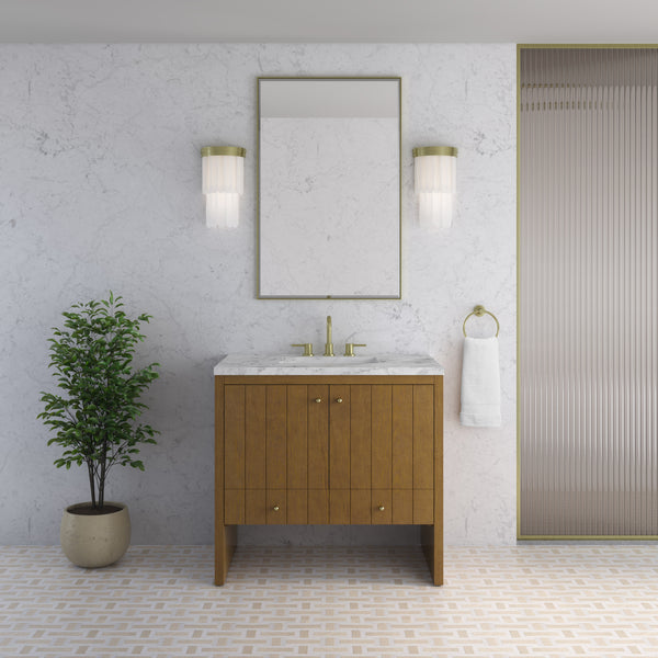 A modern bathroom featuring a striking Hudson 36″ Vanity in Honey Oak with a marble countertop, complemented by a mirror, two wall sconces, a potted plant, and a white towel hanging on a ring. The light-colored walls with subtle patterns enhance the luxury bathroom furniture, creating an elegant and inviting atmosphere.