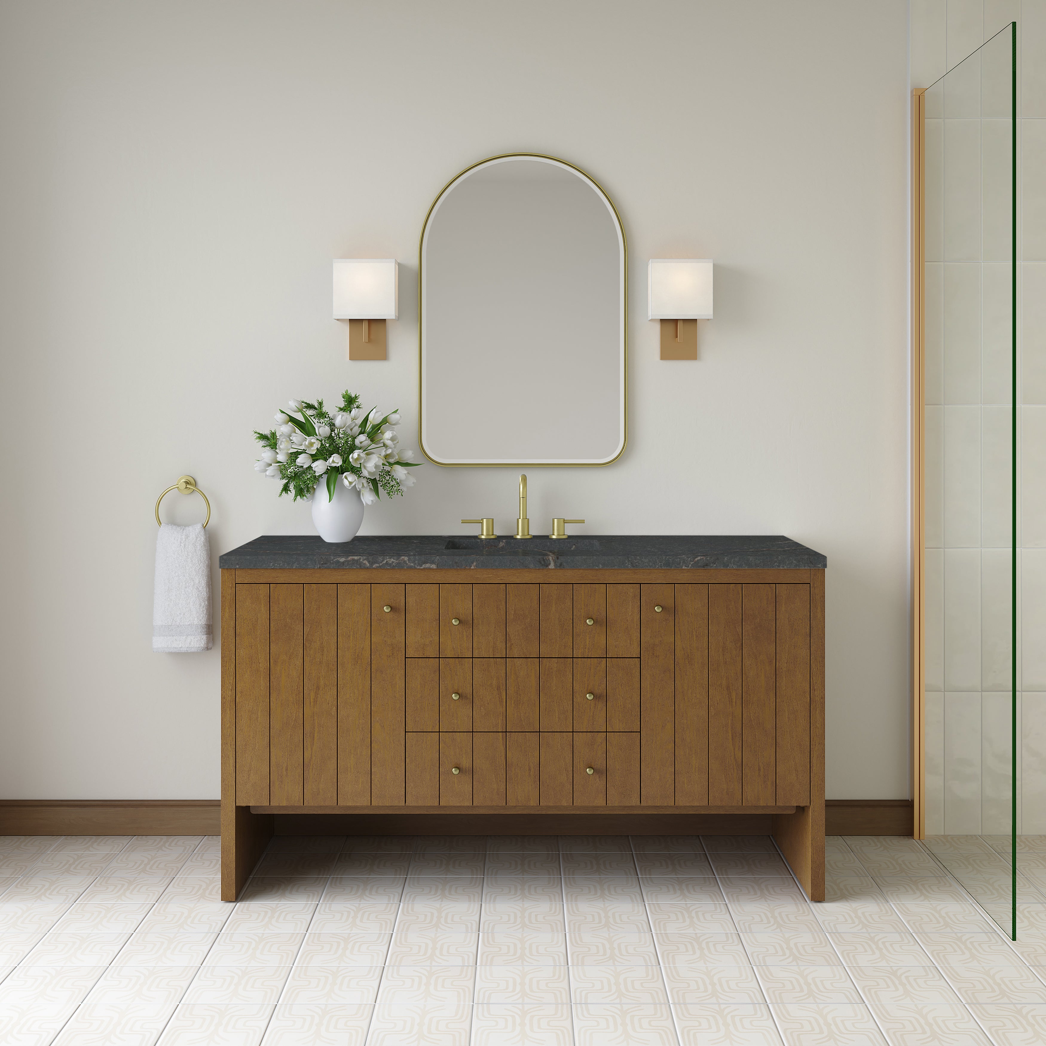 
		                            A modern luxury bathroom featuring the Hudson 60″ Vanity in Honey Oak with a sleek black countertop, brass faucet, oval mirror, two elegant wall sconces, a white vase with flowers, hand towel on a ring, and a striking patterned tile floor.
		                            