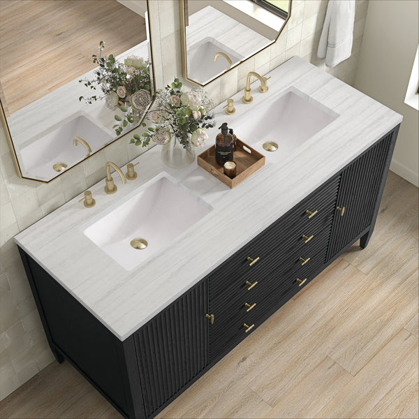 Modern bathroom vanity with a white marble countertop, two sinks, gold faucets, and dark cabinetry. A tray with soap and decor, and a vase of flowers are placed between the sinks. A large mirror hangs above.