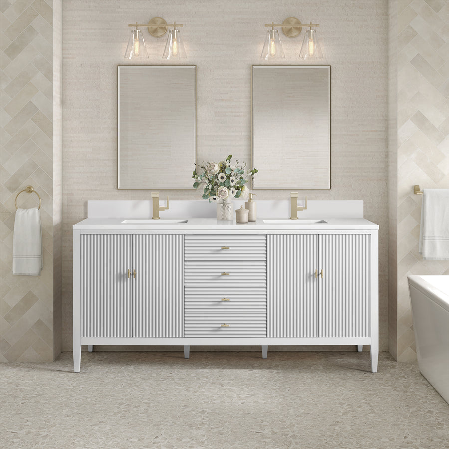 A modern bathroom with a double-sink white vanity, gold hardware, two rectangular mirrors, wall sconces, beige tiled walls, a towel ring, and a vase with white flowers on the countertop.