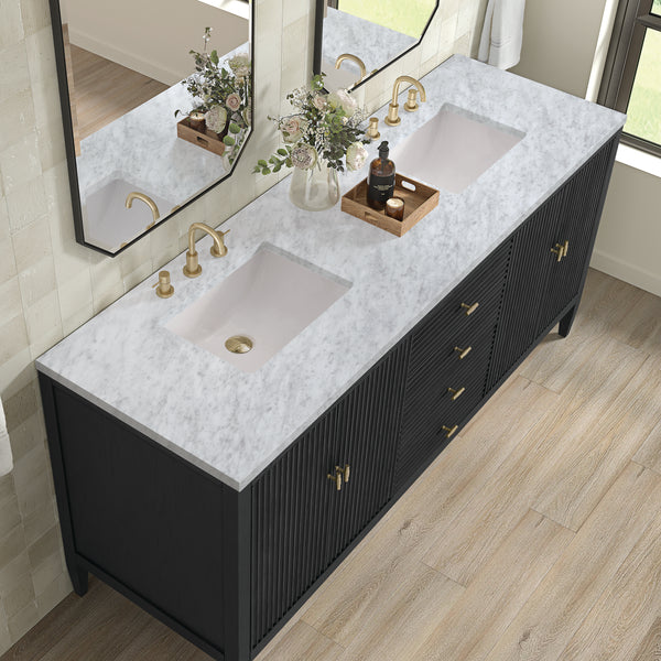Modern bathroom vanity with a white marble countertop, two sinks, gold fixtures, a vase with flowers, a tray with bottles, and black cabinets. Large mirrors and light wood flooring complete the elegant look.