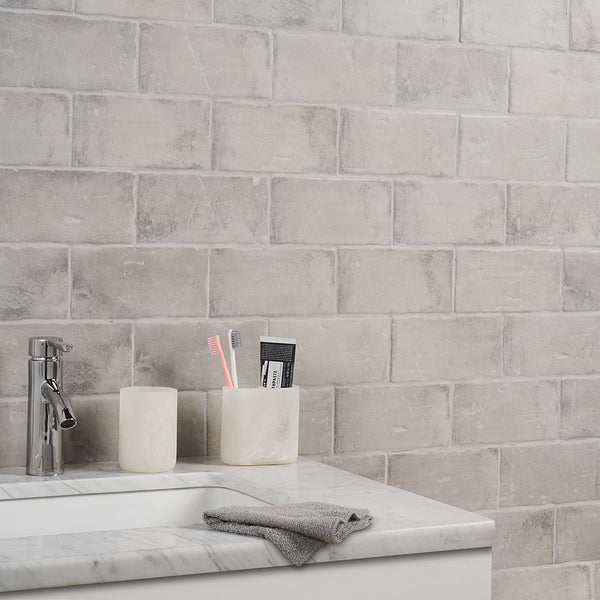 A marble bathroom counter with a silver faucet, a gray washcloth, and two marble holders—one with a pink toothbrush, a gray toothbrush, and toothpaste, and the other empty—in front of a light gray tiled wall.